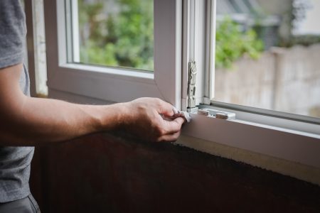 One Caucasian man in gray T-shirt cleaning lower part of window frame from dirt with paper napkin standing inside in room on spring day, side view close-up. Window cleaning concept, window frame repair, construction work.